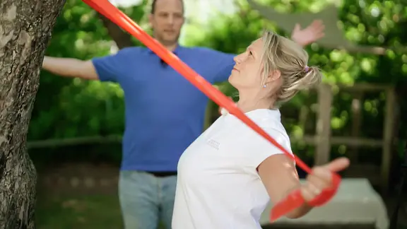 Patientin Cathrine P. führt Dehnübungen mit einem Theraband durch.