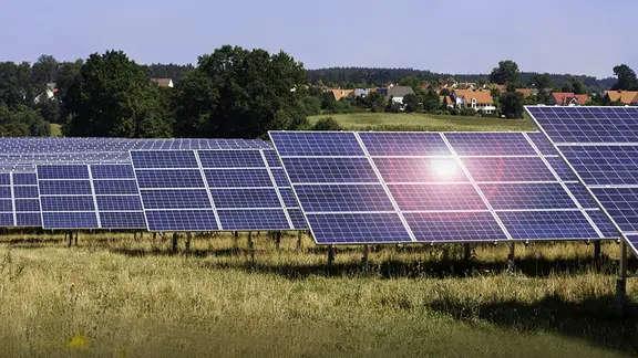 Solarpark mit Photovoltaikanlagen auf einer Wiese in ländlicher Umgebung. Die Solarmodule sind in Reihen angeordnet und nutzen Sonnenenergie zur Stromerzeugung.