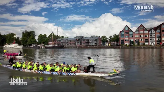 Ein Drachenboot fährt auf einem Gewässer vor einer Stadt.