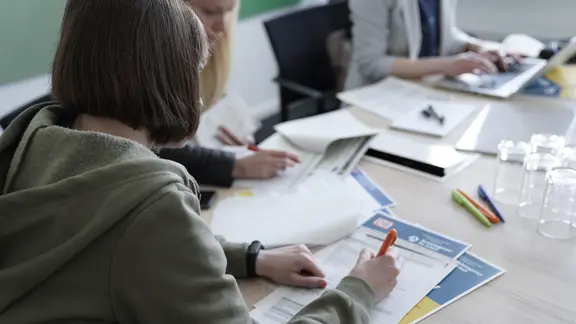 Menschen füllen an einem Tisch Formulare aus.