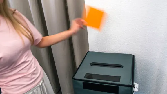 Ein Frau wirft einen Stimmzettel in eine Wahlurne