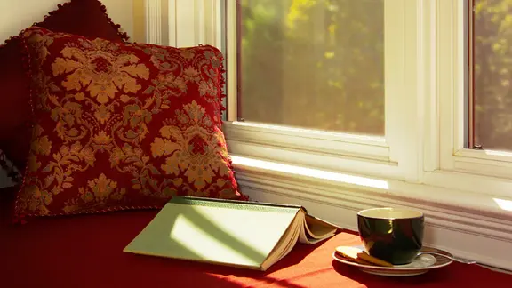 Ein aufgeschlagenes Buch liegt auf einer Fensterbank neben einer Kaffeetasse.