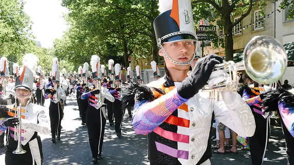 Teilnehmer in Trachten und Kostümen gehen während des Schützenausmarsches durch die Innenstadt und machen Musik.
