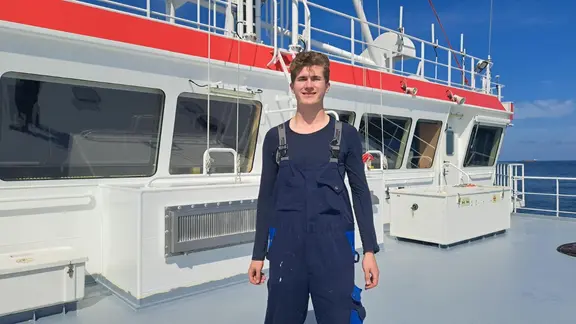 Ein junger Mann steht an Bord eines Schiffes
