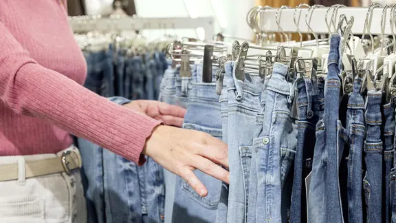 Eine Frau in einem rosafarbenen Pullover wählt blaue Jeans aus einem Kleiderständer aus.