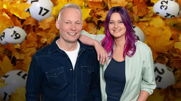 Ein Mann und eine Frau stehen vor einer Collage aus Lottokugeln und Herbstlaub.