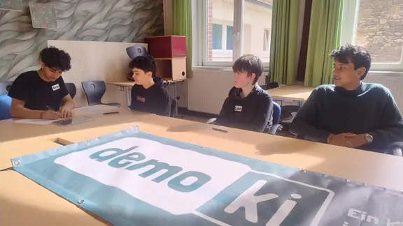 Vier Schüler sitzen in einem Klassenraum und arbeiten an einem Projekt.