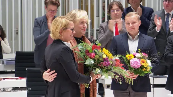 Zwei Frauen und ein Mann stehen nebeneinander im Schweriner Landtag und halten je einen großen Blumenstrauß.