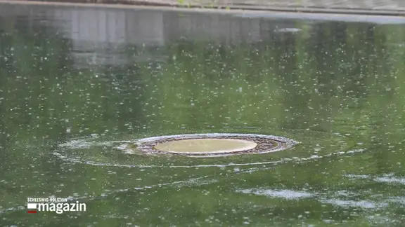 Regen fällt auf eine Straße mit Gullideckel