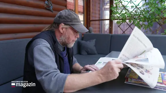 Ein älterer Mann sitzt am Tisch und guckt in eine Zeitung.