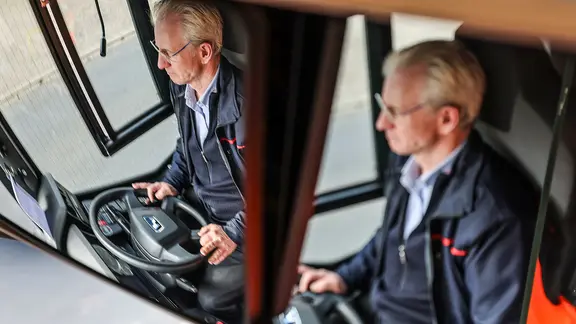 Ein Fahrer der Verkehrsgesellschaft Rheinbahn ist im Rückspiegel zu sehen, während er einen Bus durch die Stadt steuert.