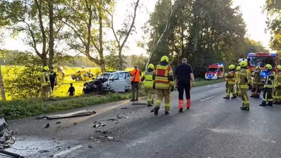 Einsatzkräfte stehen neben einem zerstörten Pkw.