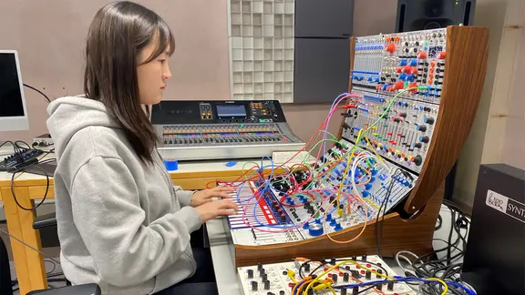 Goeun Kim sitzt vor einem analogen Synthesizer mit vielen bunten Kabeln und musiziert. 