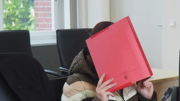 Die Angeklagte im Fall Fabian hält im Gerichtssaal eine Aktenmappe vors Gesicht.