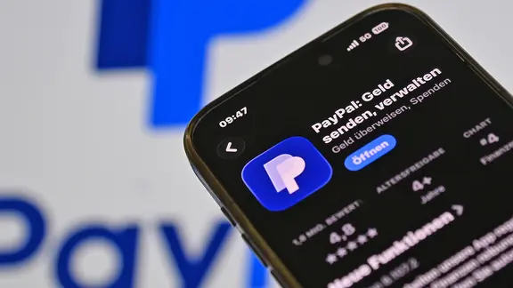 Ein Smartphone mit der Paypal-App, im Hintergrund das Paypal-Logo.