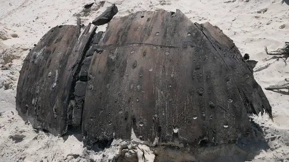 Ein stark verwittertes Stück Holz eines Schiffswracks an einem Strand.