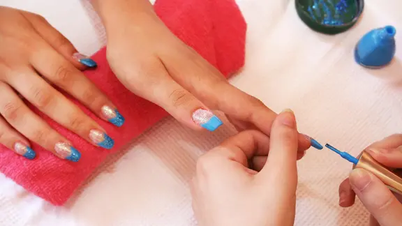 In einem Nagelstudio werden die Hände einer Frau mit blauem und transparentem Gel und Glitzer verziert.