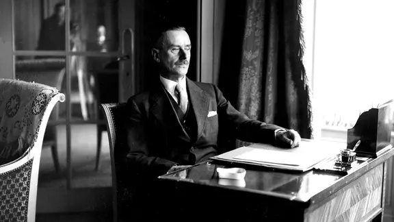 Thomas Mann sitzt an einem Schreibtisch in einem Brüsseler Hotel.