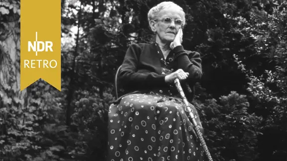 Ältere Frau sitzt auf einem Stuhl im Garten, 1950er Jahre (auf s/w gezogen).