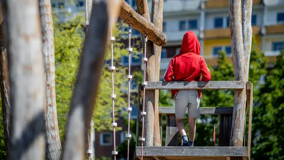 Ein Kind steht auf einem Spielplatz vor einem Plattenbau.