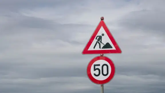 Unter einem Baustellenschild hängt ein Geschwindigkeitsschild, das ein Tempo von 50 km/h vorgibt.