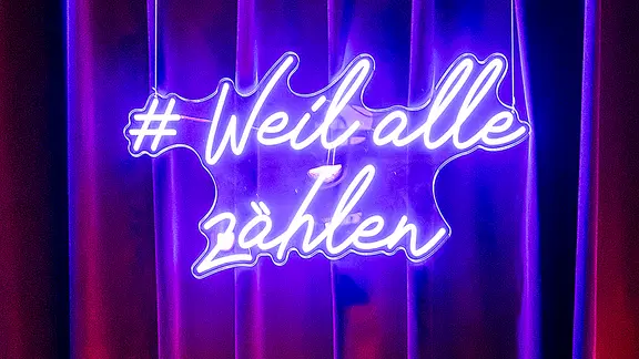 eine Leuchttafel mit der Aufschrift "#Weil alle zählen"