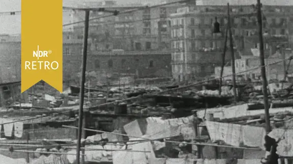 Ärmliche improvisierte Hütten, im Hintergrund mehrstöckige neue Wohngebäude (Italien ca .1960)