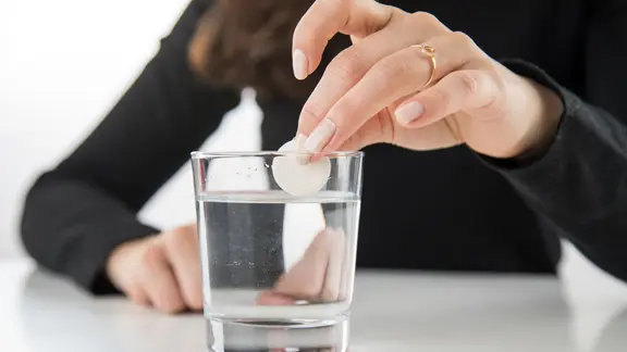 Eine Frau hält eine Brausetablette über einem Wasserglas in der Hand.