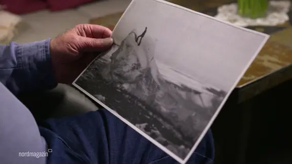 Eine Person hält ein schwarz-weißes Foto in der Hand, auf dem eine Person auf einem Eisberg steht.