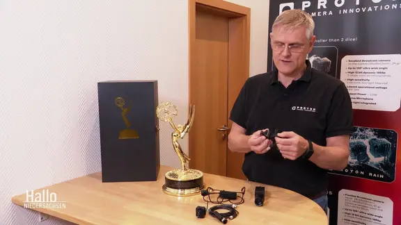 Eine Person der Firma Proton zeigt seine Kameratechnik. Auf dem Tisch steht auch die Emmy-Trophäe.