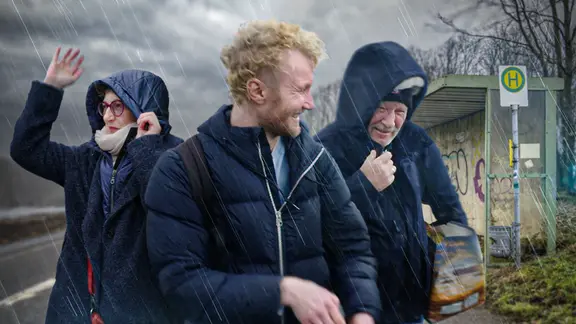Der Autor mit seinen Eltern bei Wind und Regen vor einer Haltestelle.