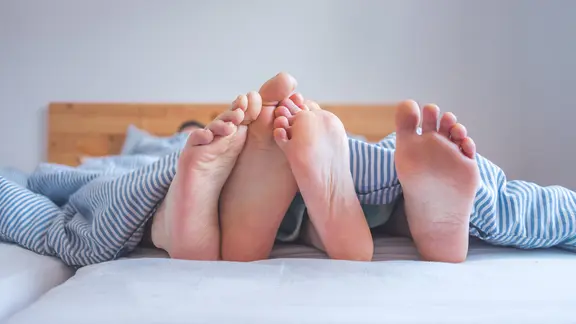 Zwei Fußpaare im Bett.
