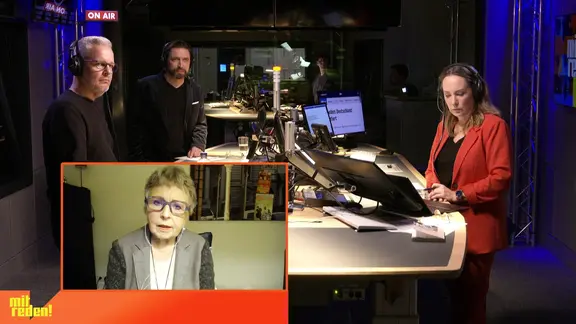 Nina Zimmermann steht mit Gesprächspartnern im Studio von NDR Info. Eine Gesprächspartnerini ist zugeschaltet.