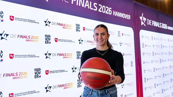Eine Frau hält einen Basketball vor sich.