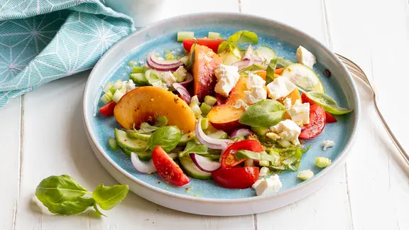 Ein Teller mit einem Salat mit Pfirsich und Feta.
