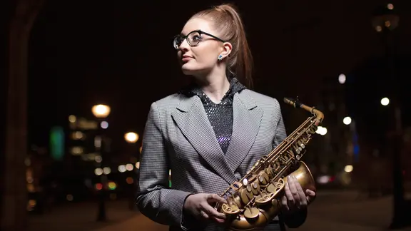 Junge Frau hält ein Saxophon in den Händen, während sie nach links blickt.