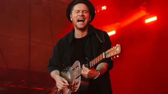 Johannes Oerding singt auf einer Bühne im roten Licht und blickt in die Kamera