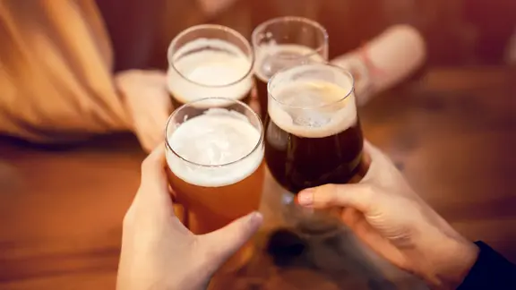 Vier Hände halten vier Biergläser und stoßen damit an.