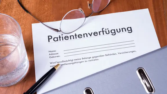 Eine Patientenverfügung liegt mit einer Brille und einem Stift auf einem Tisch.