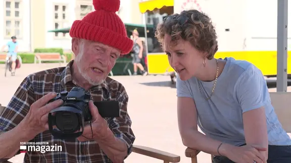 Ein Mann mit roter Pudelmütze zeigt der Reporterin Fotos auf seiner Kamera.