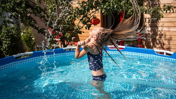 Ein Mädchen badet in einem Gartenpool, wirft ihren Kopf in den Nacken und schleudert Wasser aus ihren langen Haaren.