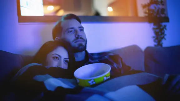 Eine Frau und ein Mann sitzen im Fernsehlicht auf einem Sofa