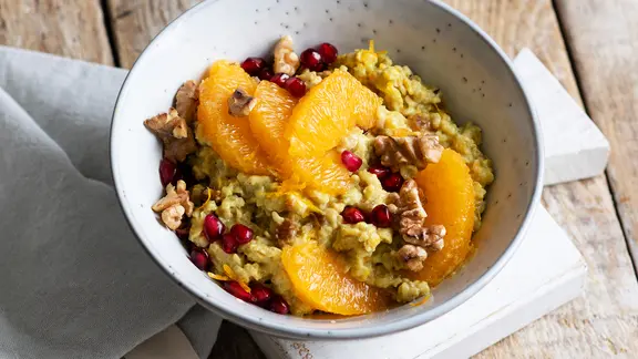 Eine Schale Porridge mit Datteln, Orangenfilets, Granatpafelkernen und Walnüssen.