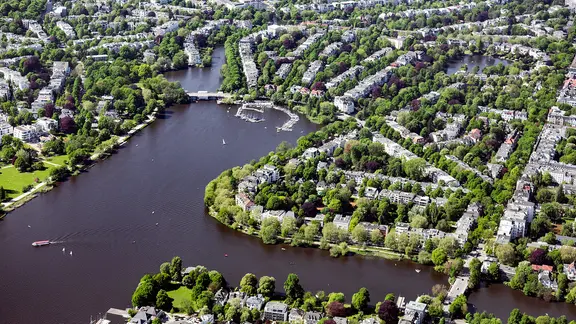 Eine Luftaufnahme des Hamburger Stadtteils Winterhude und der Außenalster mit vielen Bäumen.