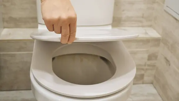 Eine Hand schließt einen Toilettendeckel.