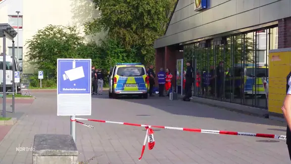 Einsatzkräfte der Polizei stehen vor einem Supermarkt. 