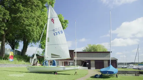 Ein Segelboot steht auf einer Wiese vor einem Haus.