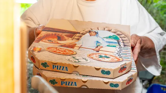 Ein Pizzalieferant bringt zwei Pizzakartons nach Hause.