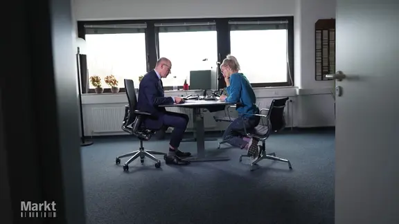 Eine Frau und ein Mann sitzen sich an einem Schreibtisch gegenüber und studieren ein Dokument.