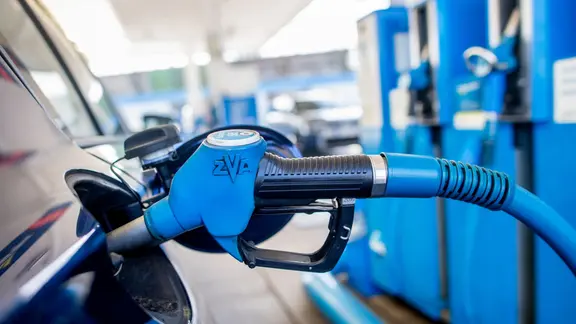 Eine Zapfpistole mit der Aufschrift "Super 95" steckt an einer Tankstelle in der Tanköffnung eines Fahrzeugs.